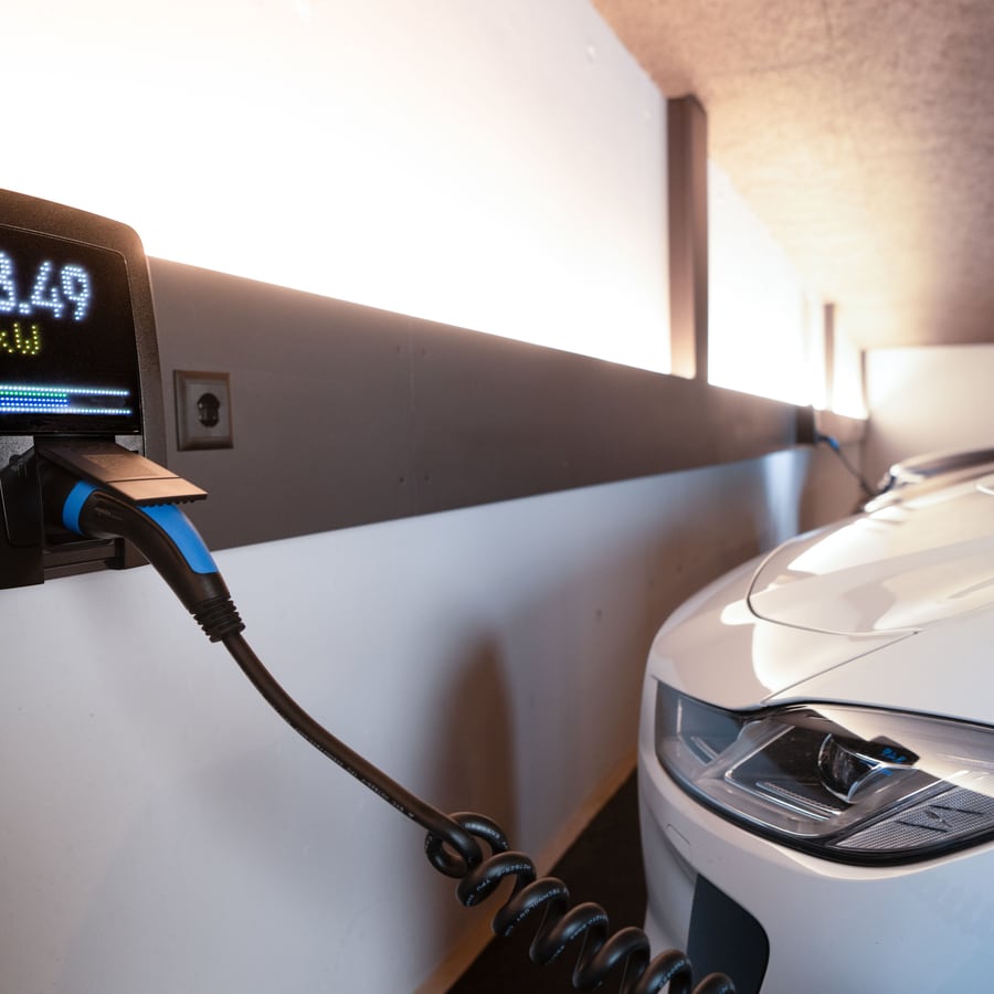 Vom Elektriker installierte Wallbox mit eingestecktem Ladekabel neben einem E-Auto in der Garage