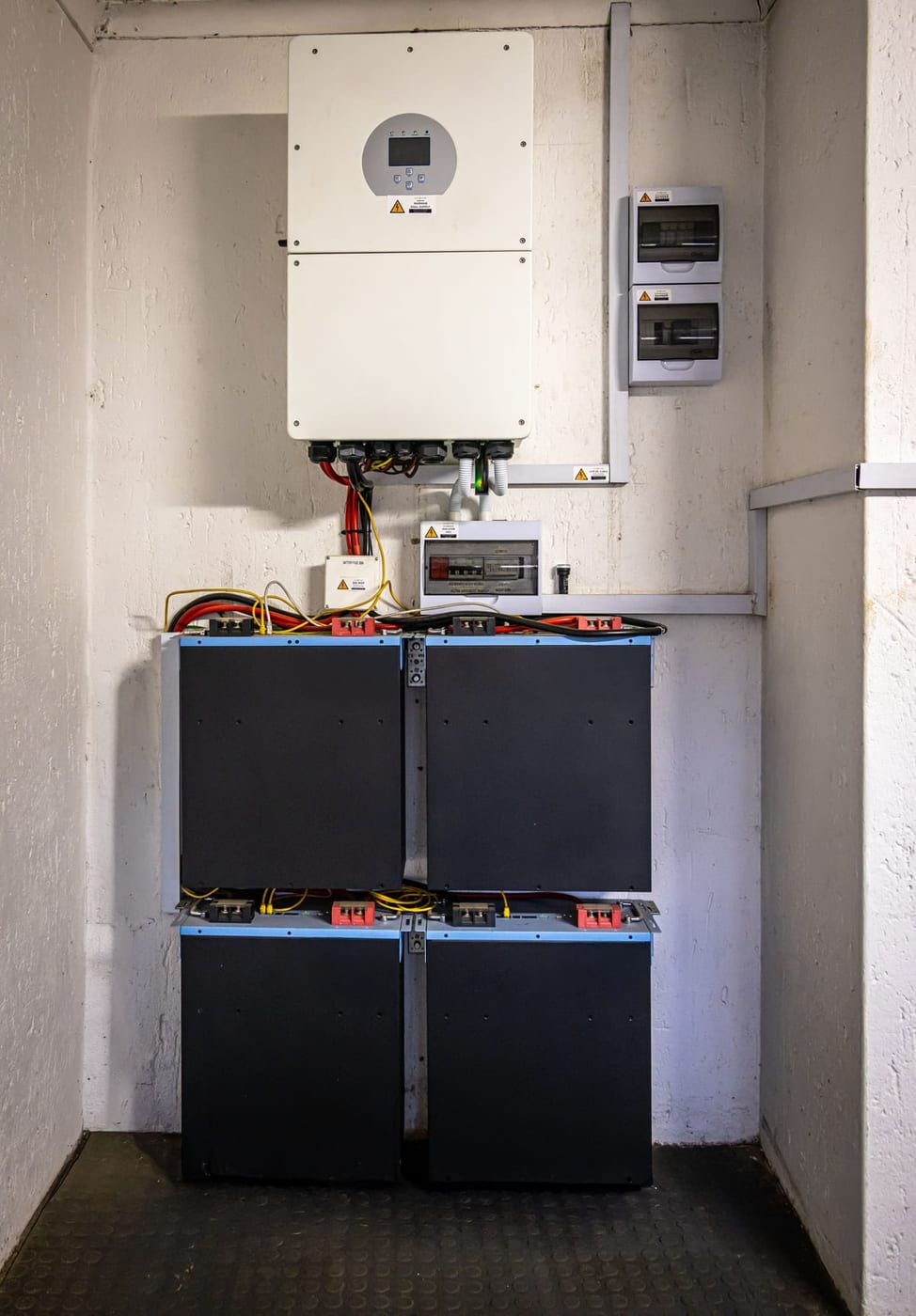 Vom Elektriker angeschlossener Wechselrichter mit darunter montierten Batteriemodulen in einem Technikraum
